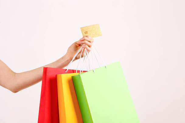 Cropped shot of female hand holding bunch of different colorful blank shopping bags with golden limitless credit card over isolated white background. Black friday sale concept. Copy space, close up. - Photo, Image
