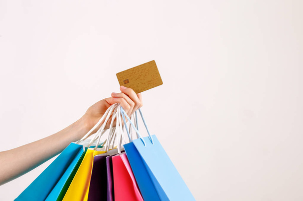Cropped shot of female hand holding bunch of different colorful blank shopping bags with golden limitless credit card over isolated white background. Black friday sale concept. Copy space, close up. - Fotó, kép