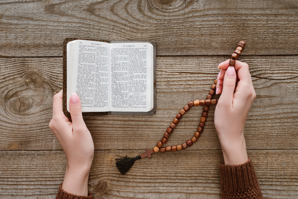 cropped shot of woman with holy bible holding beads on wooden surface - Foto, Bild