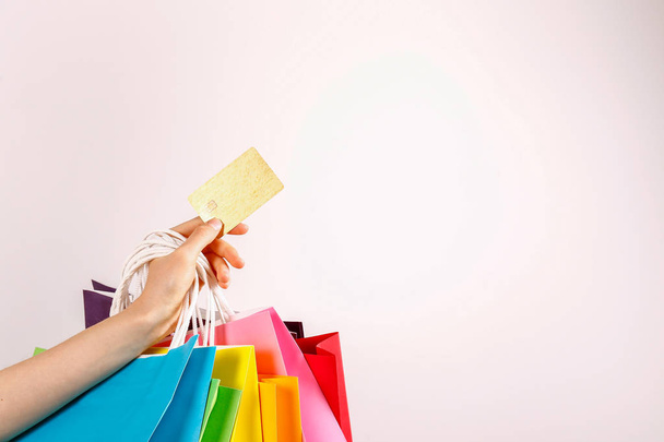Cropped shot of female hand holding bunch of different colorful blank shopping bags with golden limitless credit card over isolated white background. Black friday sale concept. Copy space, close up. - Φωτογραφία, εικόνα