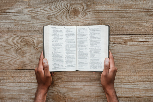 cropped shot of man holding holy bible over wooden table - Photo, Image