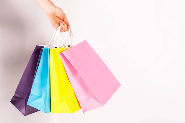 Cropped shot of female hand holding bunch of different colorful blank shopping bags over isolated white background. Many packets with in woman's arms. Black friday sale concept. Copy space, close up. - Fotó, kép