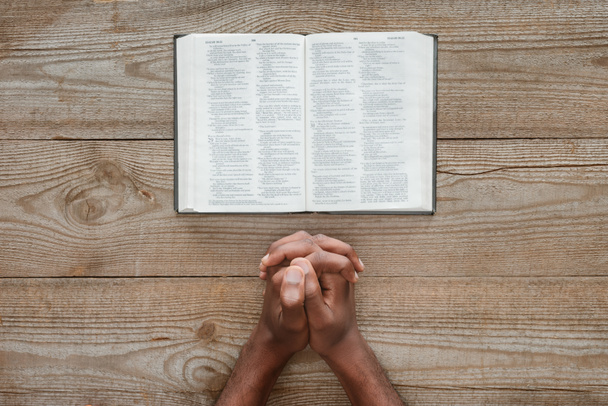 cropped shot of african american man praying with holy bible on rustic wooden table - Photo, Image
