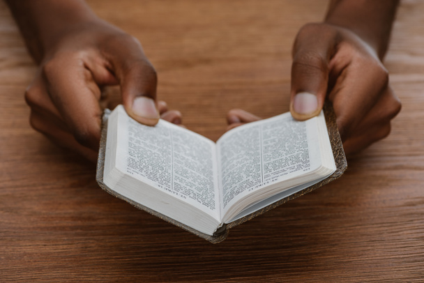 cortado tiro de homem afro-americano lendo bíblia sagrada na mesa de madeira
 - Foto, Imagem