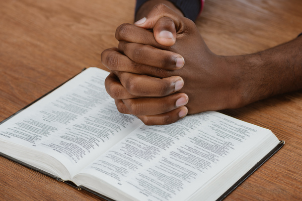 cropped shot of african american man praying with holy bible on wooden table - Photo, Image