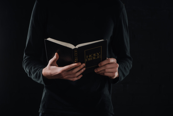 cropped shot of priest reading holy bible isolated on black - Foto, Imagem