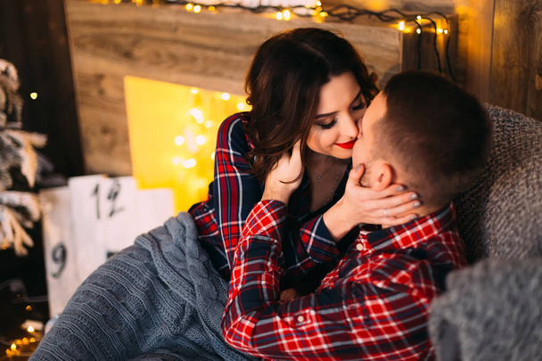 chico y chica quieren besarse sentado en un sillón suave y cubierto con una manta en una acogedora habitación cerca de la chimenea
 - Foto, imagen