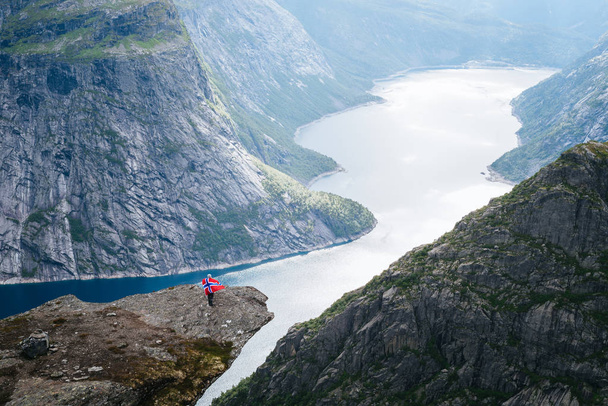 ノルウェーの最も人気のある 1 つのハイキングします。Ringedalsvatnet 湖があります。Trolltunga の崖からの眺め。ノルウェー国旗を持つ少女 - 写真・画像