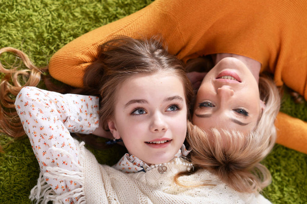 Happy mother with  daughter  lying on green carpet at home - Photo, image