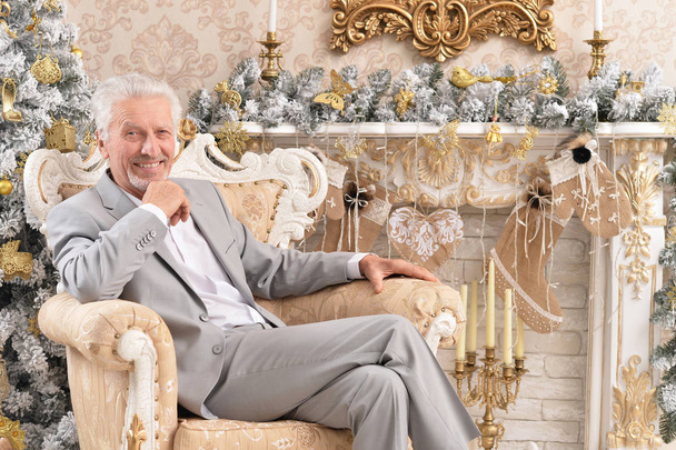 Portrait of confident senior businessman sitting in chair in room decorated to Christmas holiday - Photo, image
