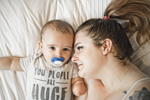 Portrait of beautiful mom playing with her 8 months old baby in bedroom, top view - Foto, Imagen