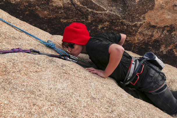 Fit young caucasian woman with red hat and sunglasses rock climbs in the desert - Photo, Image