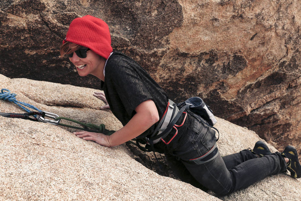 Kırmızı şapkalı, güneş gözlüklü beyaz bir kadın çöle tırmanıyor. - Fotoğraf, Görsel