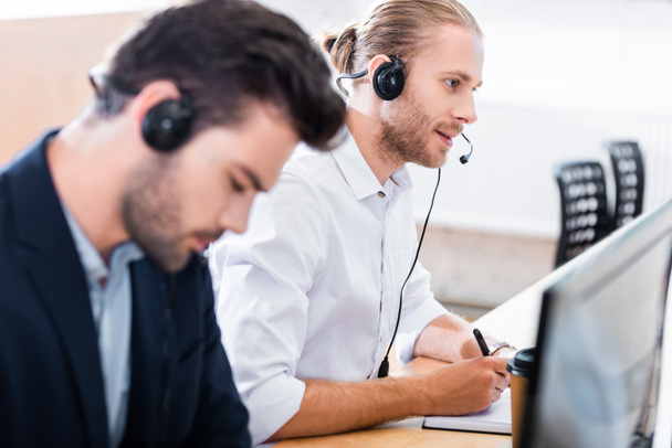 selective focus of male call center operators in headsets at workplace in office - 写真・画像