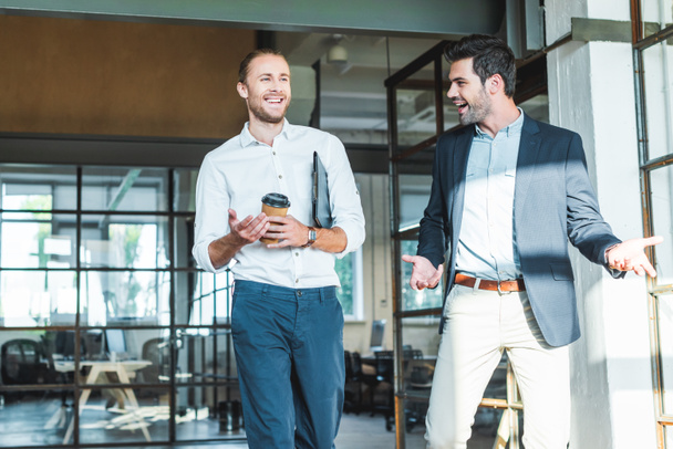 sonrientes colegas de negocios conversando mientras caminan en el pasillo
 - Foto, Imagen