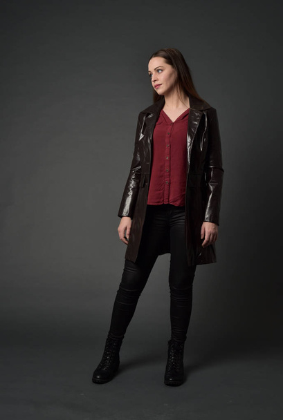 ritratto a figura intera di ragazza bruna che indossa un lungo jack di pelle rossa. posa in piedi su sfondo grigio studio
. - Foto, immagini