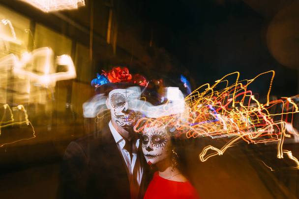 blur of foranium, ghosts of the dead, long exposure. A man and a woman with a visage, a pattern of skulls, a zombie on the face. Dead at night. A pair of zombies in the dark outside, blurry lights, ghosts. The day of the dead and Halloween. long expo - 写真・画像