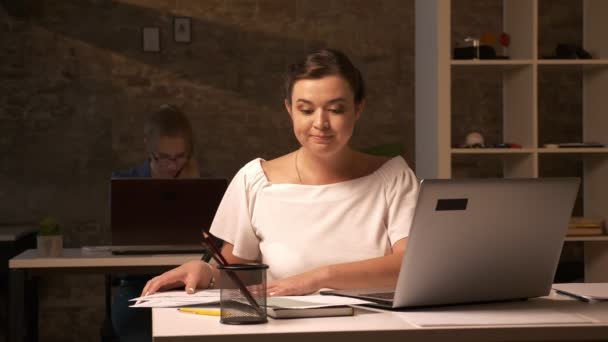 Focused thinking face on caucasian business girl who is harmonising her documents, sitting at workplace with laptop - Video, Çekim