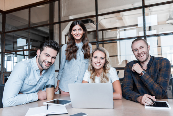 щасливі молодих бізнес колег працюють із пристосунками і посміхатися камери в офісі   - Фото, зображення