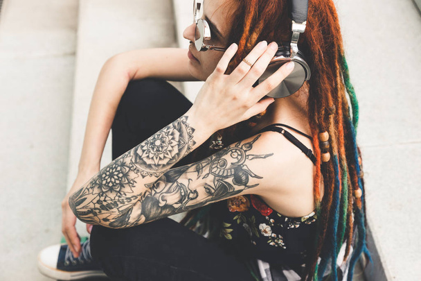 young girl with tattoo and dreadlocks listening to music while sitting on the steps. - Foto, Bild
