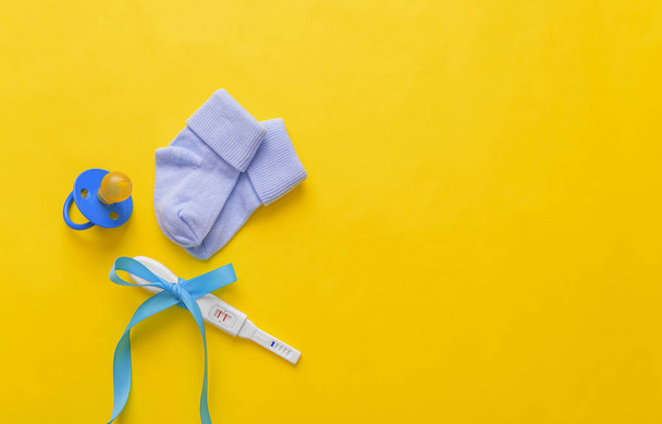Baby socks and a pregnancy test on a yellow background. - Zdjęcie, obraz