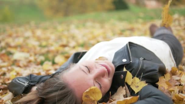 Krásná mladá žena leží v žluté listí pod stromem. - Záběry, video