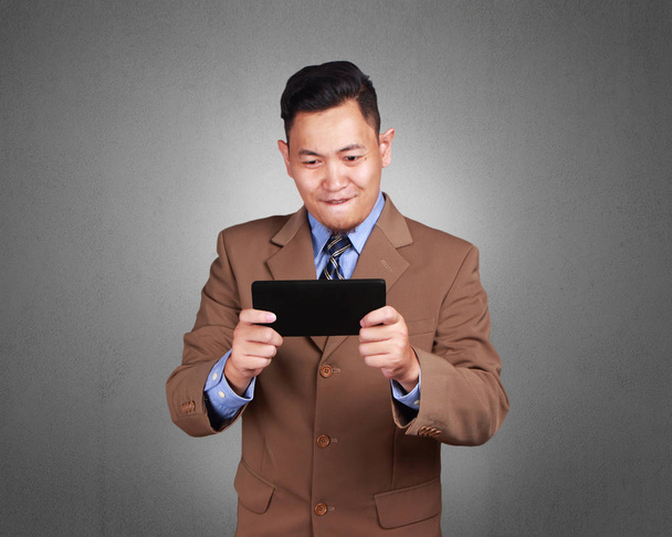 Portrait de jeune homme d'affaires asiatique heureux jouant sur sa tablette, surfant sur les bonnes nouvelles, jeux en ligne, activité de loisirs, sur fond de grunge
 - Photo, image