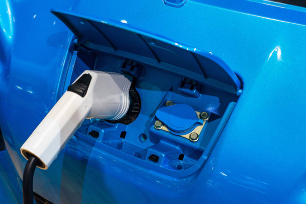 White electric car charger plug nozzle on a blue car - 写真・画像