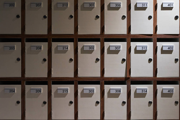 Свет и тень небольших закрытых почтовых шкафчиков с номерами комнат
 - Фото, изображение