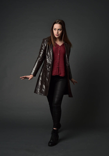 full length portrait of brunette girl wearing  red long leather jack. standing pose on grey studio background. - Photo, Image