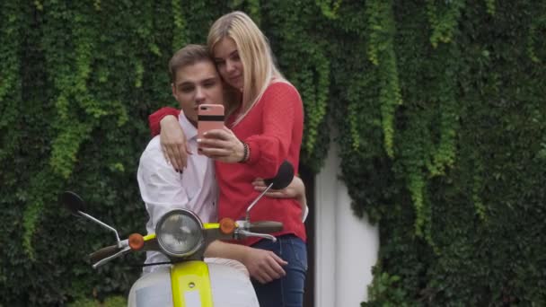 Beautiful couple makes a selfie on the motorbike. Guy on a moped hugs a girl. A girl and a guy are posing on the phone. - Footage, Video