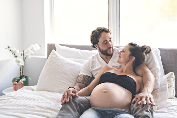 Man with pregnant woman in bed at home having great time - Photo, Image