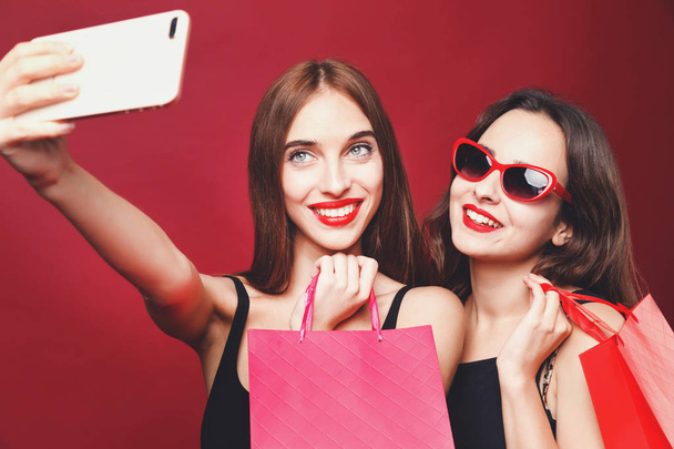 Two Girlfriends Holding Paper Shopping Bags And Making Selfie - 写真・画像