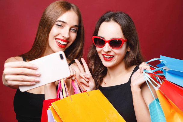 Two Girlfriends Holding Paper Shopping Bags And Making Selfie - Foto, imagen