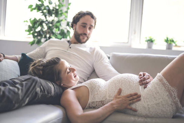 Young happy Couple expecting baby on sofa - Fotoğraf, Görsel