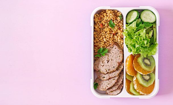 Almuerzo saludable con bulgur, carne y verduras frescas y frutas sobre un fondo rosado. Concepto de fitness y estilo de vida saludable. Una lonchera. Vista superior
 - Foto, imagen