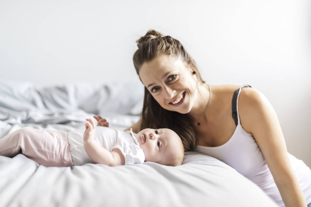 Portret van een mooie moeder met haar 2 maanden oude baby in de slaapkamer - Foto, afbeelding