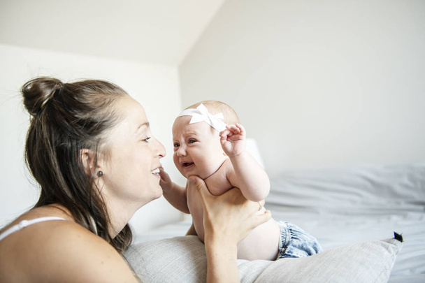 Portrait of a beautiful mother with her 2 month old baby in the bedroom - Photo, Image