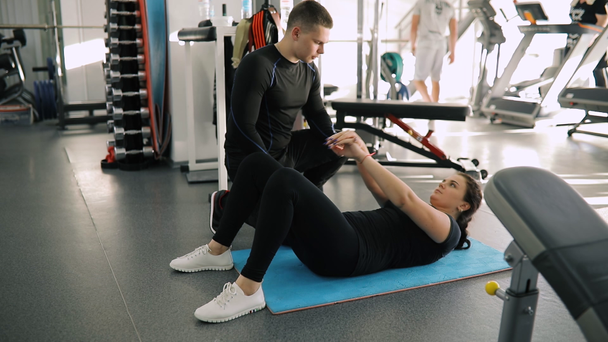 Персональный инструктор по фитнесу тренирует начинающую спортсменку в спортзале, пока она качает живот
 - Кадры, видео