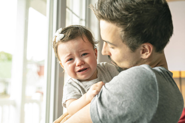 Father holding little girl close to the window, unhappy girl cry - 写真・画像
