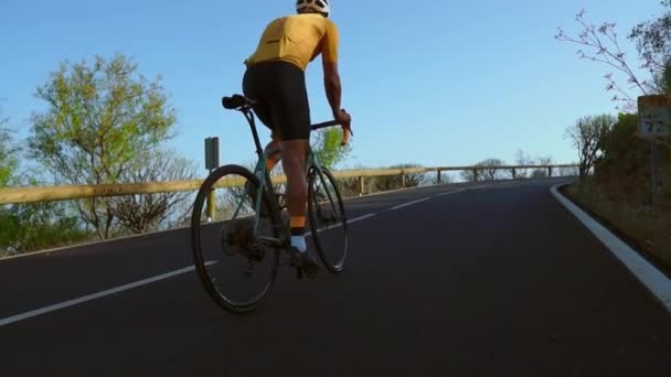 Bir adam yolda bisiklet binmek. Spor ve aktif bir yaşam konsepti günbatımı zamanı. Bir adam bir parkta bisiklet sürme. Bisikletçi vücut üzerinde turuncu güneş ışını ile mavi gökyüzü. - Video, Çekim
