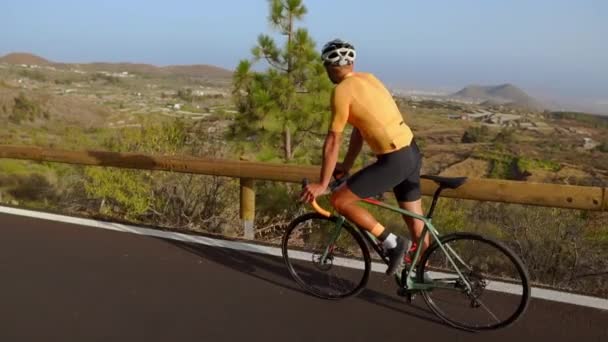 Відстеження відеозапису чоловічої велосипедистки, що піднімається на гірську дорогу. Чоловік займається велотренінгом на горбистій шосе в сонячний день
. - Кадри, відео