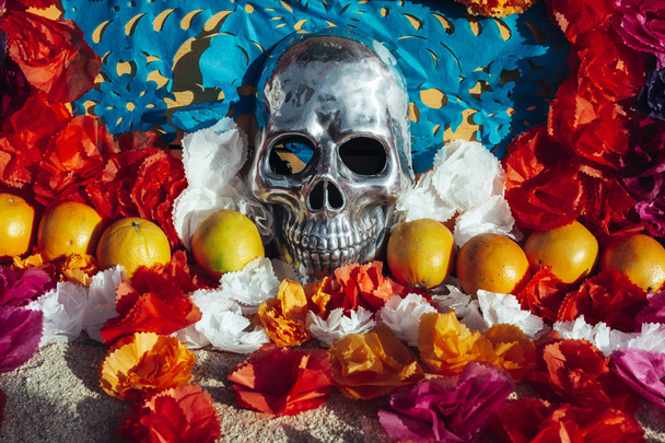 Calavera humana cromada, rodeada de flores y frutas de papel, altar mexicano
 - Foto, imagen