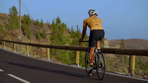 Weitwinkelaufnahme eines fitten männlichen Athleten, der mit dem Fahrrad auf einer langen flachen Straße in der Landschaft unterwegs ist. Mann radelt auf flacher Autobahn. - Filmmaterial, Video