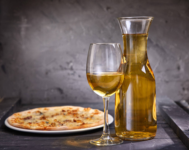 wineglass and decanter with cold white wine and pizza on wooden background, close-up   - Фото, зображення