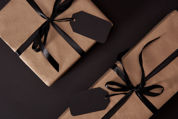 top view of craft wrapped gift boxes with black tags on black surface, black friday concept - Foto, Bild
