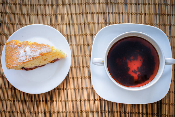Plum sponge cake over a cup of hot tea on a straw bedding - Foto, imagen