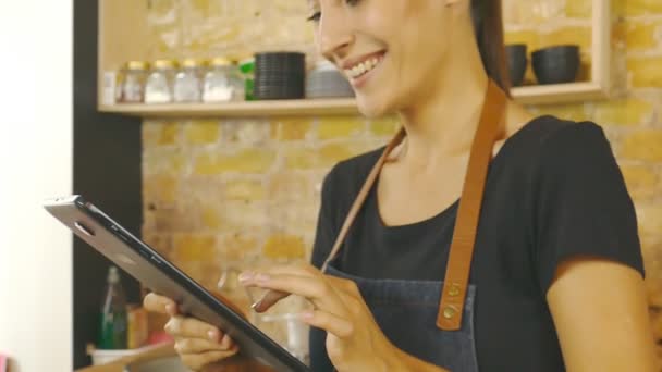 Een aantrekkelijk meisje (de eigenaar van een koffiehuis) werkt op een tablet. Slow motion. - Video