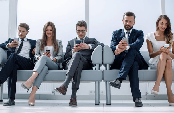 business colleagues with their smartphones sitting in the office hallway - Foto, imagen
