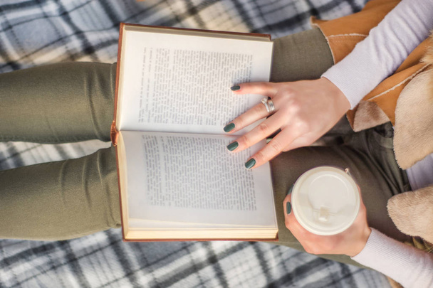 Donna con libro sulle gambe e caffè in mano. Ragazza che legge libro su coperta retrò. Immagine di concetto di autunno. Focus ravvicinato e selettivo
 - Foto, immagini